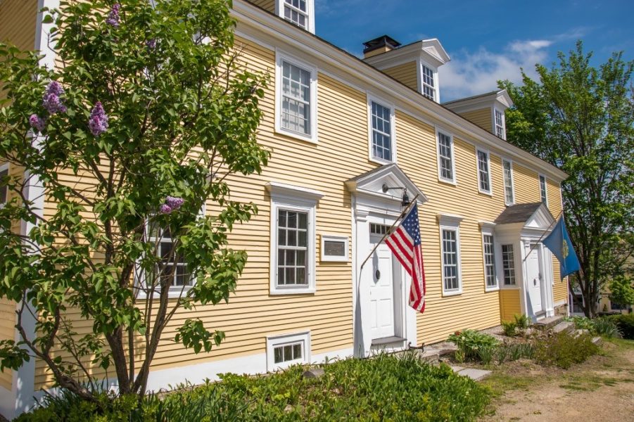 Yellow Colonial House with the American flag hanging out front.