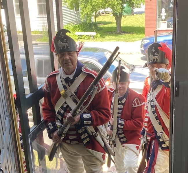 Men in British military uniforms from the 18th century stand in the Folsom Tavern doorway, ready to storm the building.