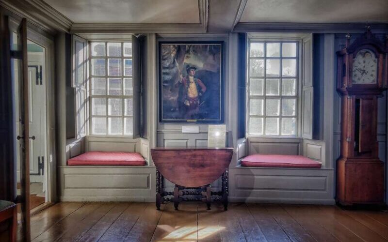 Wall of a room with two large windows. Hanging on the wall between them is a painting of General Sullivan.