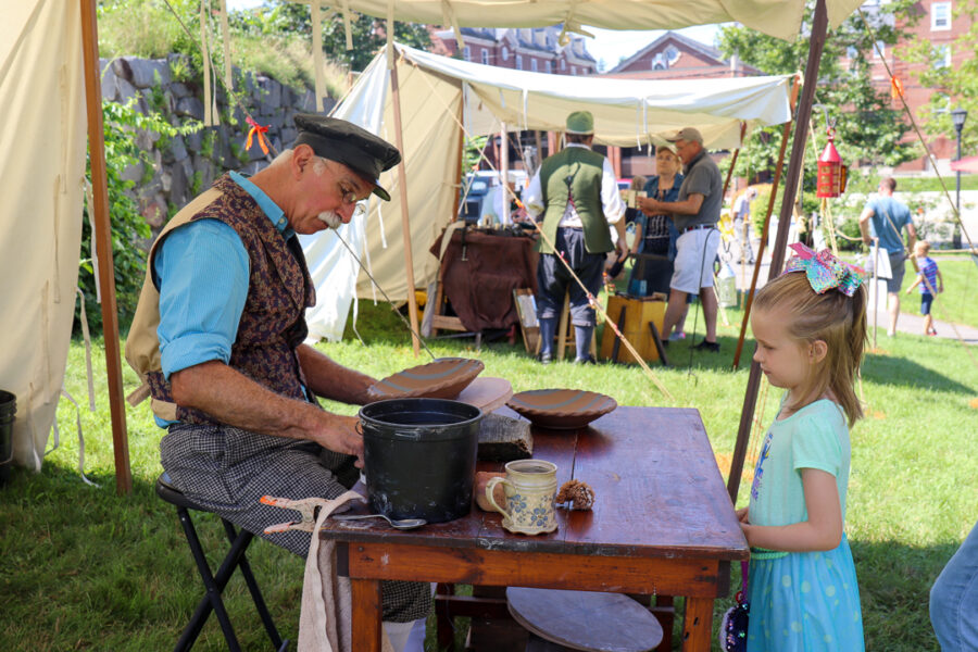 A child watches as a trained artisan decorates an unfired clay bowl using a specially cut sponge as a stamp