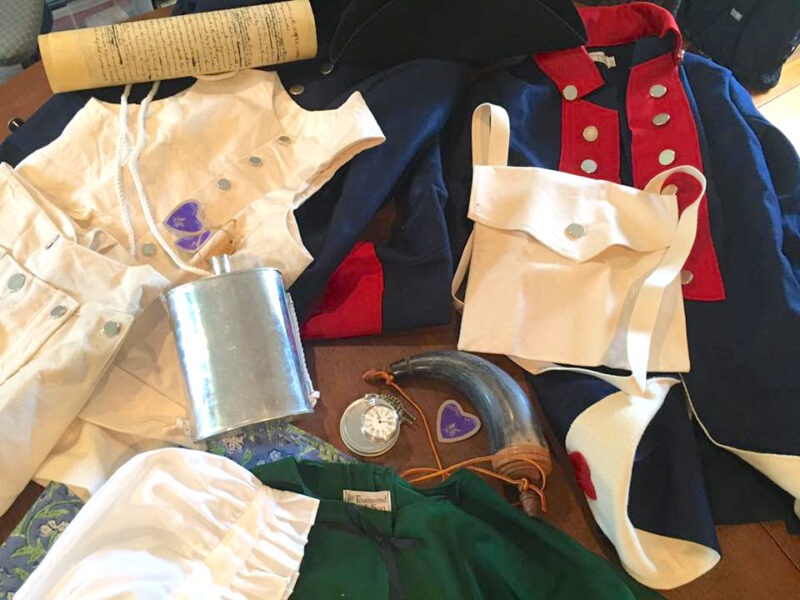 Reproduction Items from the 18th century including a canteen, clothes, and military medals.