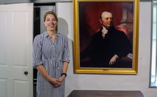 Museum Directo Emma Stratton in front og a large oil portrait of John Taylro Gilman
