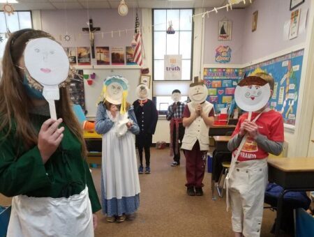 Elementary school aged children holding up paper plate masks with Revolutionary Era characters drawn on.