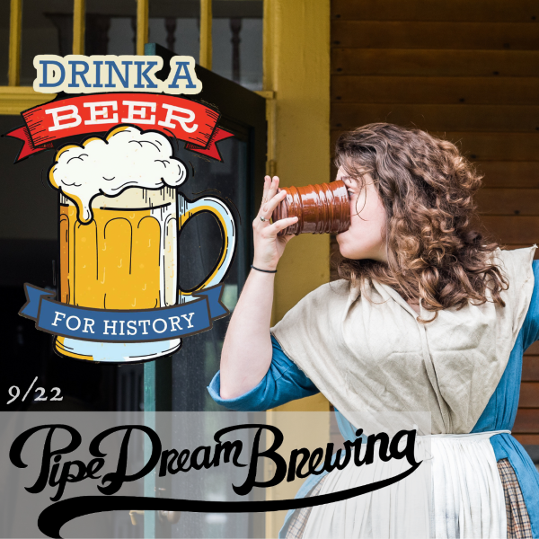 Woman in an 18th century blue dress with a white fichu over it drinks beer from a ceramic mug.