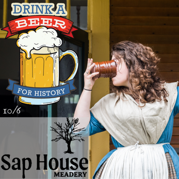 Woman in an 18th century blue dress with a white fichu over it drinks beer from a ceramic mug.